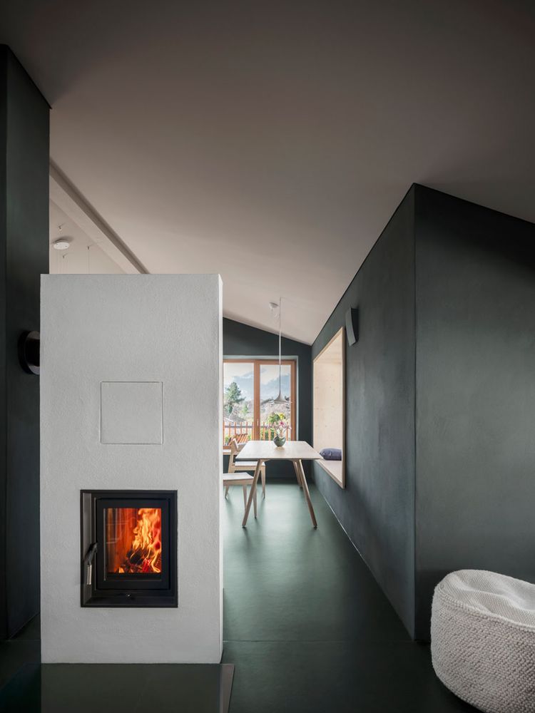 Im Kamin im Vordergrund brennt Feuer. Im Hintergrund ist der Esstisch zu sehen. Die Wände sind mit Naturfarben gestaltet.